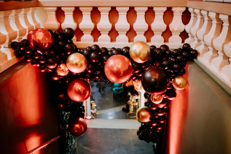 Stunning black, red, and gold balloon arch adorning a staircase, creating a dramatic and elegant ambiance for a festive celebration or upscale event. Perfect for striking entrances