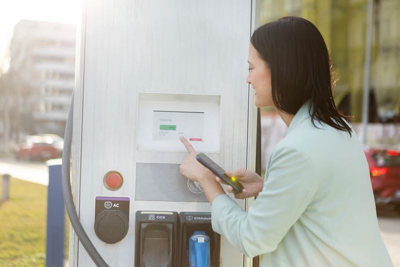 Woman charging an electric car. About 35 years old, Caucasian female.