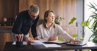 A couple working together on paperwork at a wooden table with a laptop.
