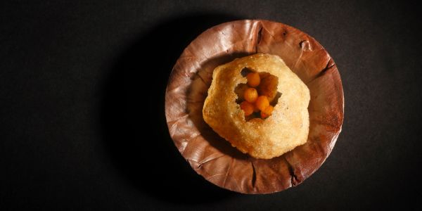 A plate with a single Indian snack item on a dark background.