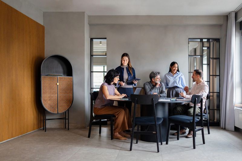Diverse business team collaborating around a round table in a bright, modern office, smiling and discussing ideas.