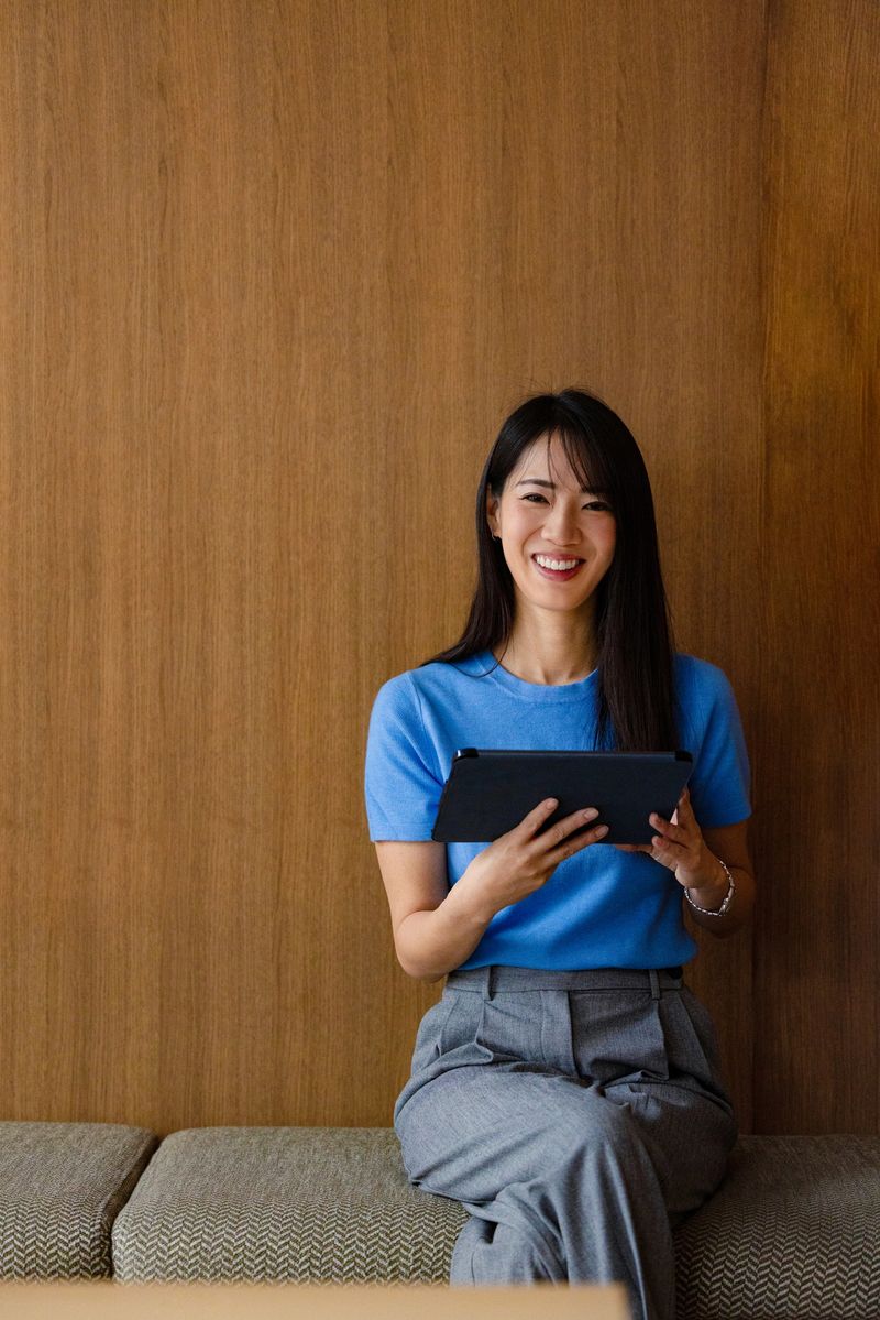 Smiling professional woman uses a tablet against a wooden wall, conveying modern business and remote work.