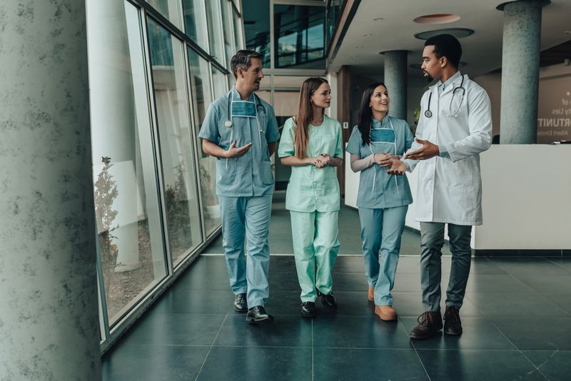 Medical team of doctor and nurses walk through modern hospital corridor while discussing patient care, teamwork and clinical collaboration during daytime shift, conveying professionalism, support and confidence.