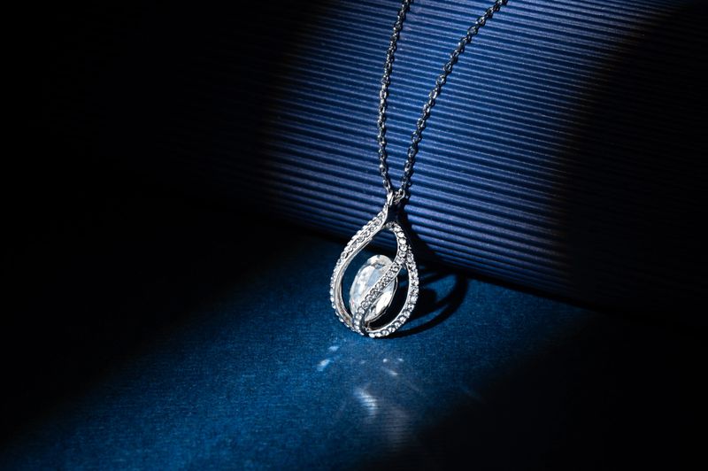 A stunning silver diamond pendant necklace glistens on a dark blue surface, illuminated by soft light casting a sophisticated shadow, ideal for luxury jewelry advertising or editorial use.