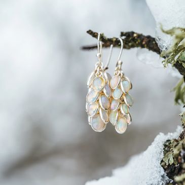 Delicate opal earrings hanging on a snowy branch.