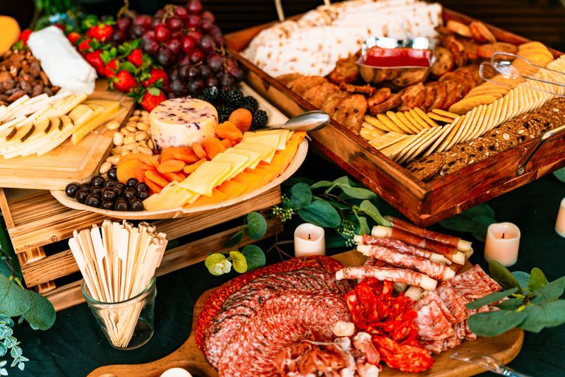 High-end charcuterie grazing table featuring cured meats, salami, rolled prosciutto, assorted cheeses, crackers, dried fruits and nuts arranged on wooden boards. Premium catering display suitable for corporate events, weddings, holiday parties and upscale entertaining concepts.