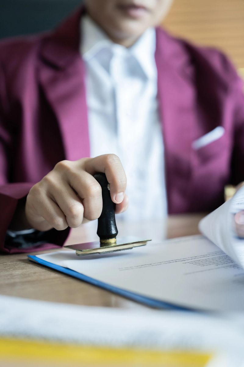 A woman is stamping a document with a stamp. The stamp is black and gold. The woman is wearing a red jacket
