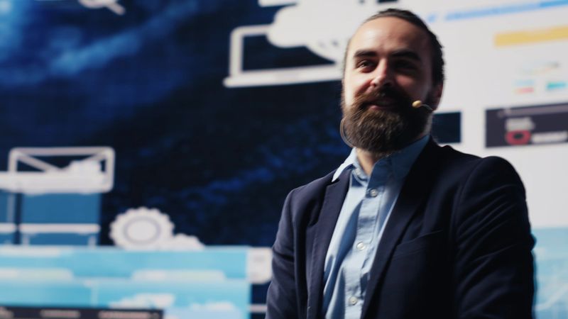 Male entrepreneur leading a visionary business pitch at the convention, inspiring the audience to fund important project. Businessman public speaker giving a speech for the crowd. Camera A.