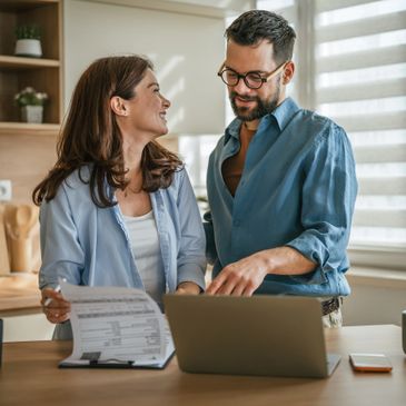 Couple discussing finances with documents and laptop in a bright kitchen.