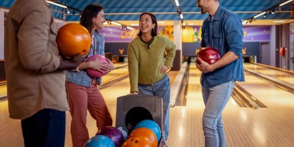 Four friends smiling and holding bowling balls at a bowling alley.