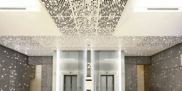 Modern elevator lobby with perforated ceilings and walls.
