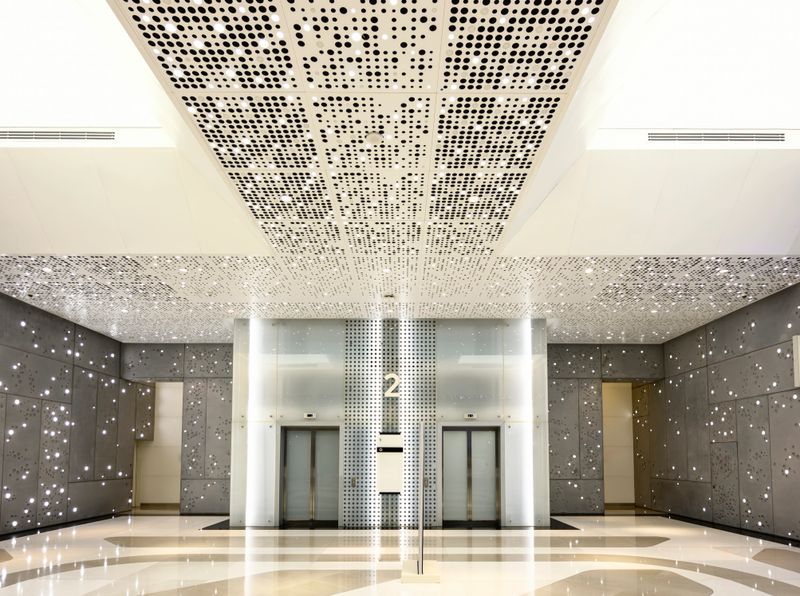 Modern elevator lobby with minimalist white and gray surfaces, perforated ceiling panel and embedded wall lights creating a futuristic, elegant corporate interior ambiance