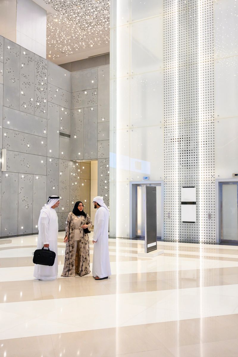 Three business professionals discussing corporate matters in a modern office atrium, featuring contemporary architecture, bright interior lighting, and sleek design elements