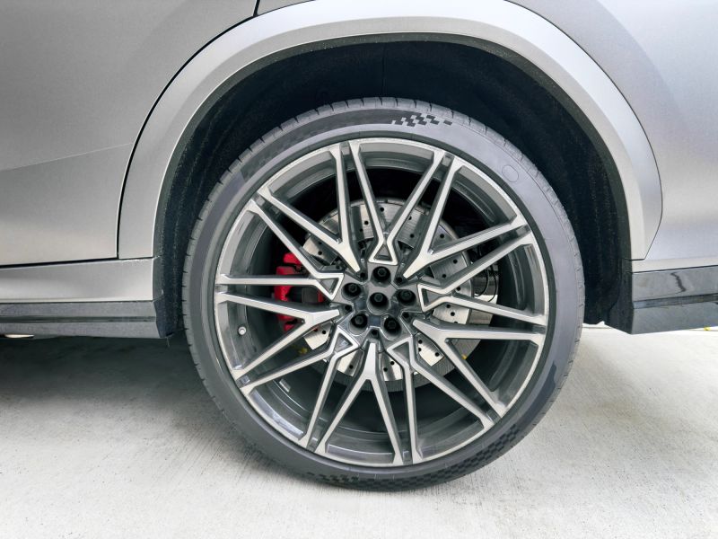 Close up view of a modern sports car rear wheel featuring a black alloy rim and performance tire parked on a gray asphalt surface. This clean automotive detail shot is ideal for themes like car design, tuning, safety, maintenance, and premium transportation in advertising or editorial projects. Horizontal composition with copy space on the road texture, suitable for web, print, and social media campaigns.