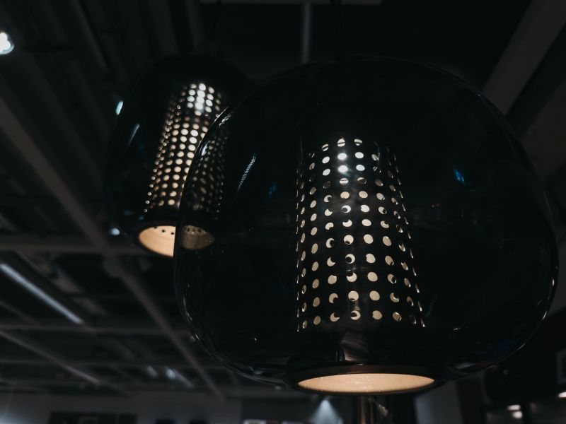 Modern black pendant lamps with perforated metal design in dark interior. Contemporary lighting creating moody atmosphere in stylish indoor space