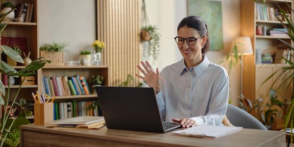 Woman smiling and waving at her laptop during a video call.