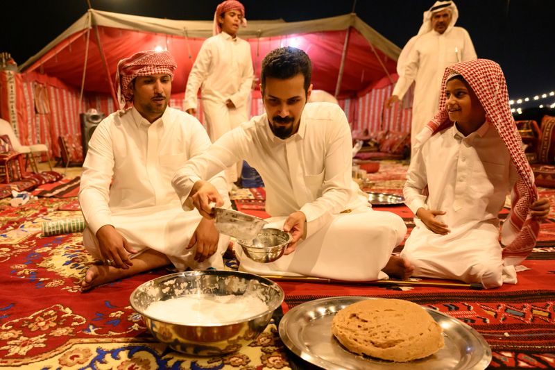Saudi family sharing traditional food and drink inside a Bedouin tent at night, enjoying Arabian hospitality, cultural bonding and conversation over a communal meal in the desert