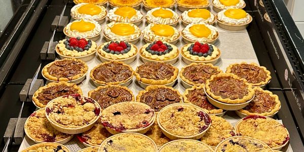 Assorted mini tarts and pies arranged in rows on a cooling rack.
