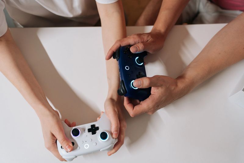 Close-up top view of young adult couple holding wireless game controllers, playing video games together, sharing leisure time and entertainment at home, enjoying fun competitive hobby.