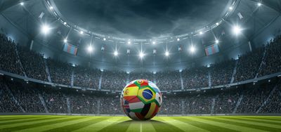A soccer ball with international flags in a packed stadium under bright lights.