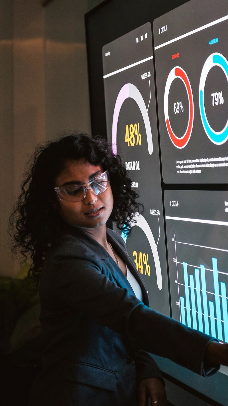 Two professionals review a large interactive analytics dashboard, discussing charts and metrics on a touchscreen in a modern office.