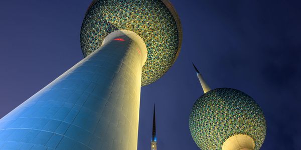 Illuminated Kuwait Towers at night against a dark sky.