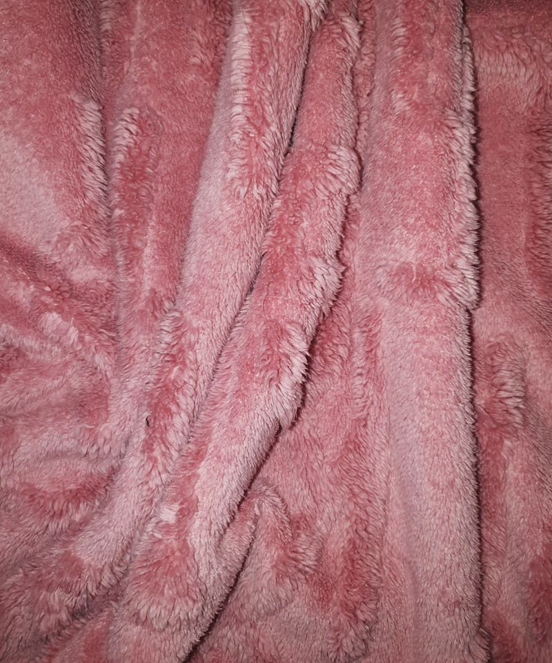 Close-up of soft pink faux fur fabric texture with waves and shadows. Minimalist abstract background for fashion, cozy lifestyle, winter comfort, and feminine design.