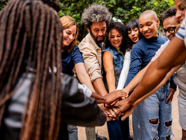 A diverse group of people joining hands in unity outdoors.