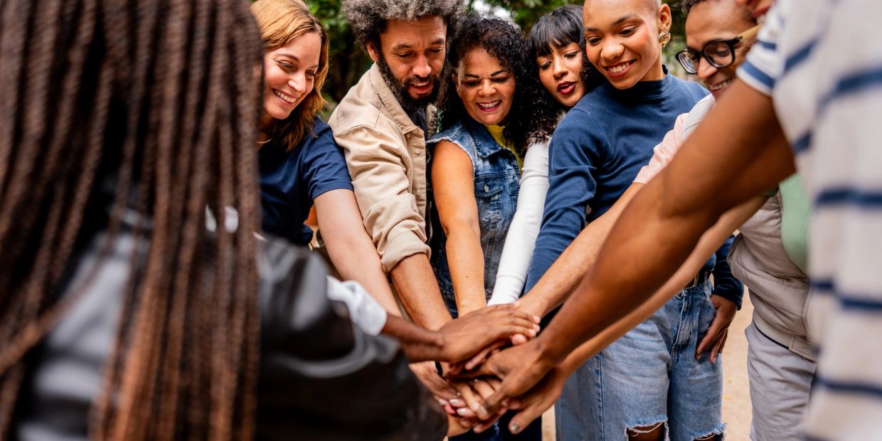 Group of friends stacking hands in unity outdoors.