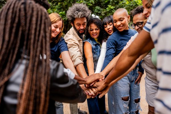 A diverse group of friends stacking their hands in a show of unity outdoors.