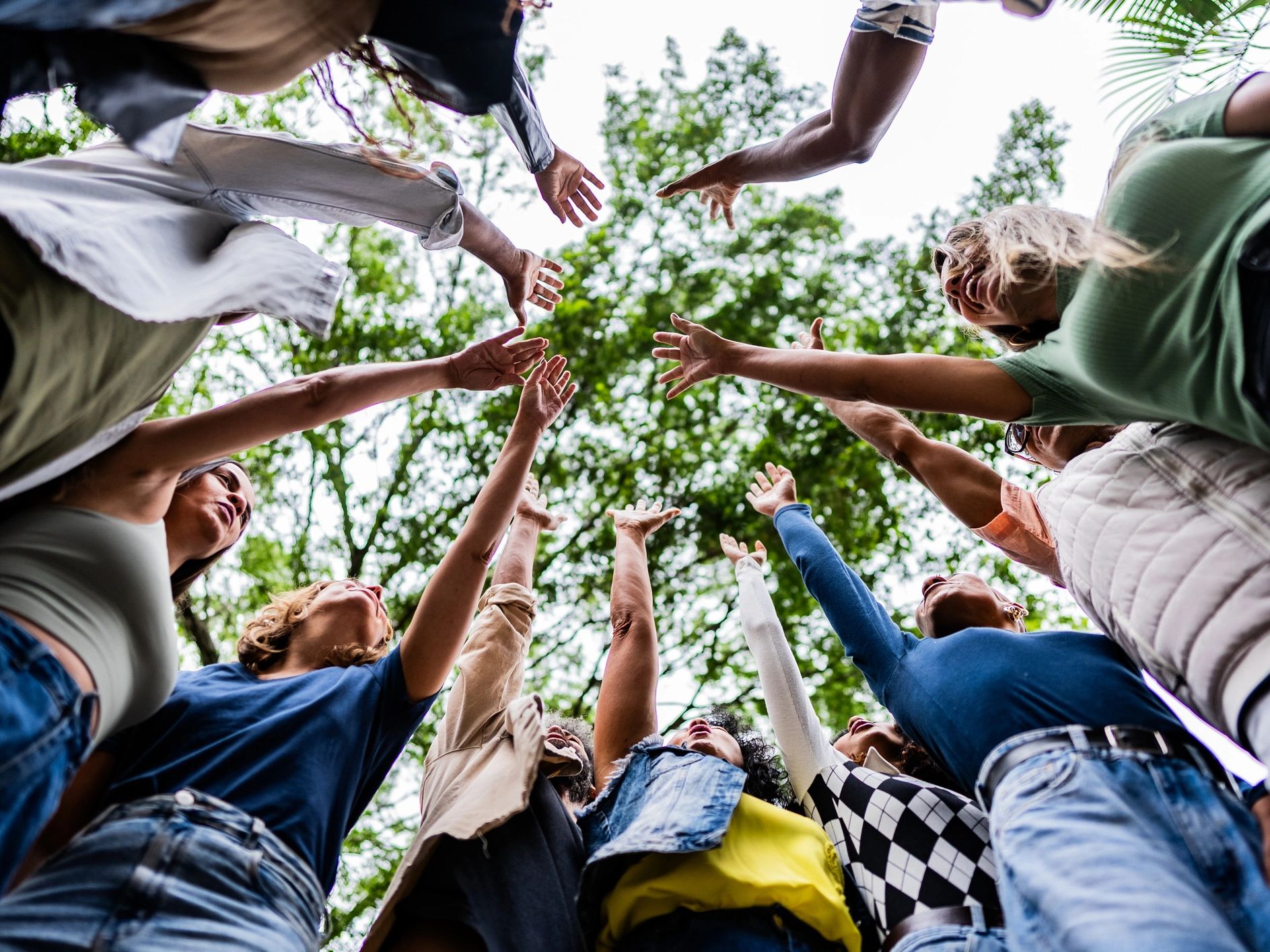 Group of people raising hands in a circle outdoors.