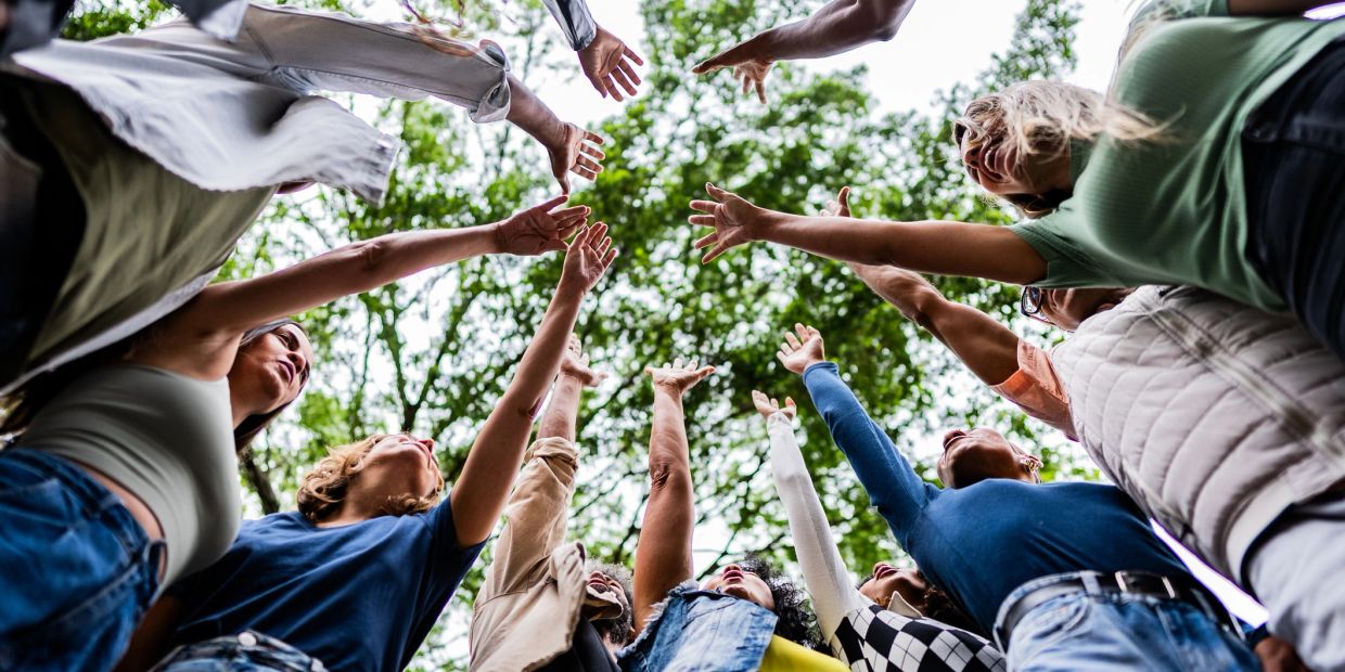 Group of people reaching upwards together outdoors.