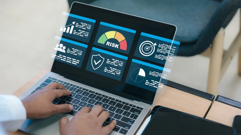 Close up of a businessman hands typing on a laptop computer keyboard with virtual holographic risk assessment dashboard and data analytics icons on screen at office workspace.