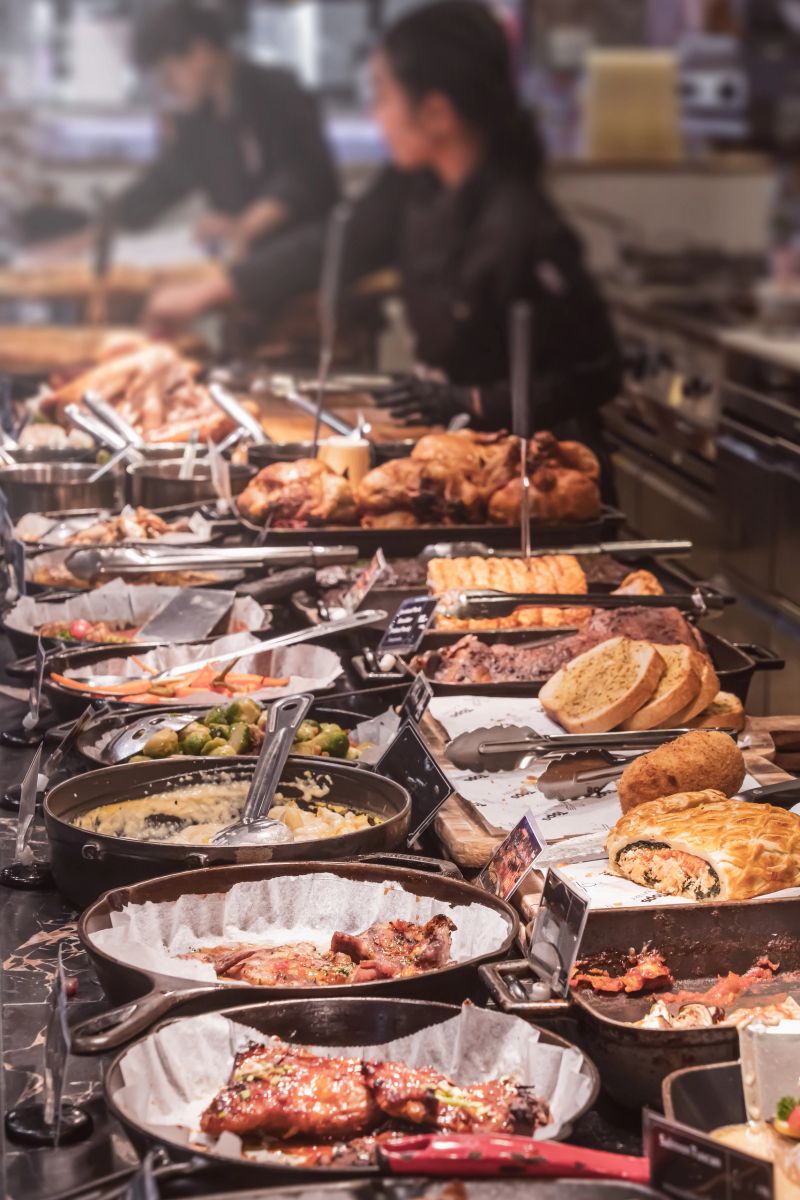 A rich selection of dishes at the Luxury Buffet restaurant located in the shopping center This is not a food court in the usual sense, but a premium buffet restaurant. In the foreground of the photo, baked meat, side dishes and pastries are visible, which are typical of the meat station and the hot snacks area of this establishment.