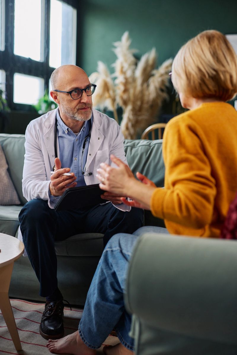 A family physician visits a senior woman at home, discussing her health and treatment plan in a warm, comfortable living room setting that conveys trust, care, and patient-centered healthcare.