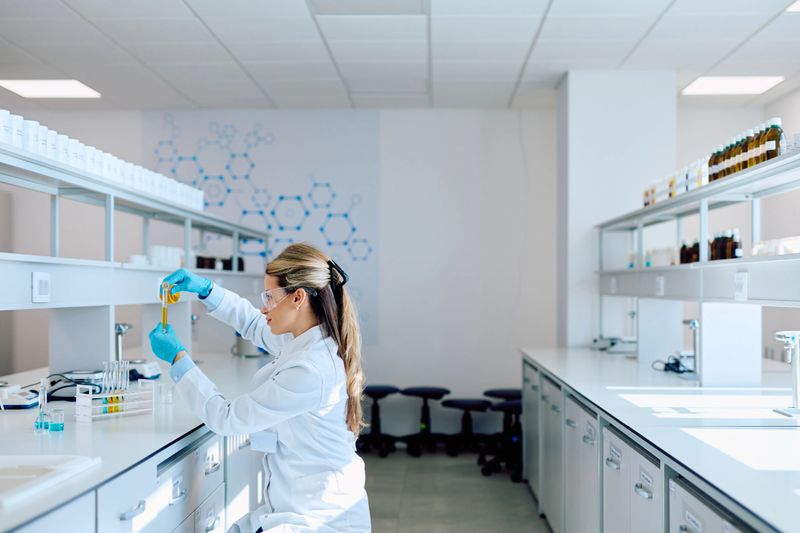 Female scientist wearing gloves and safety glasses, analyzing liquid samples in test tubes for medical research and chemistry experiments