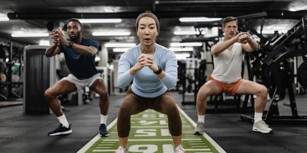 Three people doing squats together in a gym.