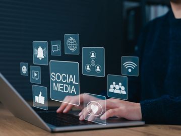 Person using laptop with social media icons floating above keyboard.
