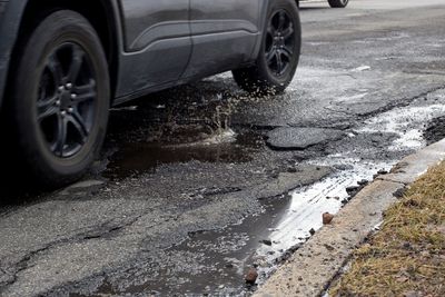 Car driving over a wet pothole on a rough road.