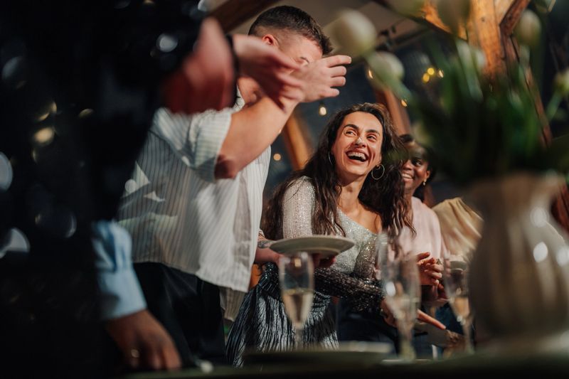 Radiant young woman in a glitzy sequin dress beams with joy as she mingles with friends at a festive gathering, embracing the spirit of celebration and creating lasting memories