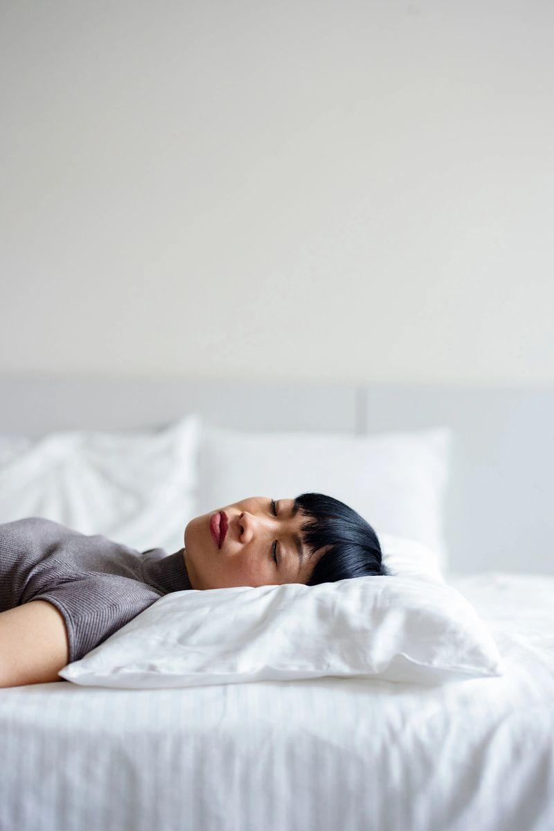 A young woman rests peacefully on a white pillow in a bright minimalist bedroom, conveying calm and relaxation.