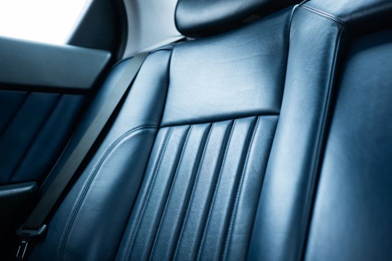 Close-up of a luxury vehicle's navy blue leather interior, featuring elegant vertical ribbed stitching and a seatbelt. Low, wide angle view, no people