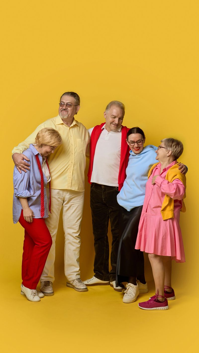 Senior friends standing arm in arm on yellow background in casual outfits. Concept of lifestyle media, active aging, social unity, healthcare communication, wellbeing visuals.