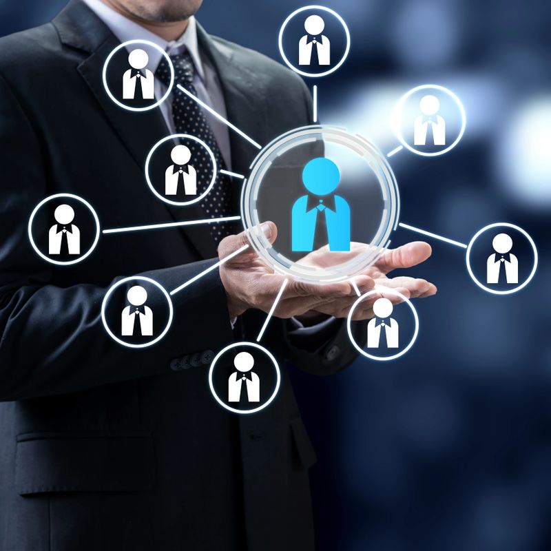 A businessman in a suit holds a digital interface featuring a central blue icon connected to multiple team members, representing human resources, leadership, and professional networking