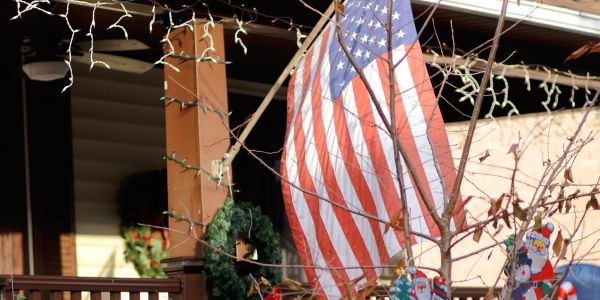 American flag flies outside a decorated porch with wreaths and holiday lights.
