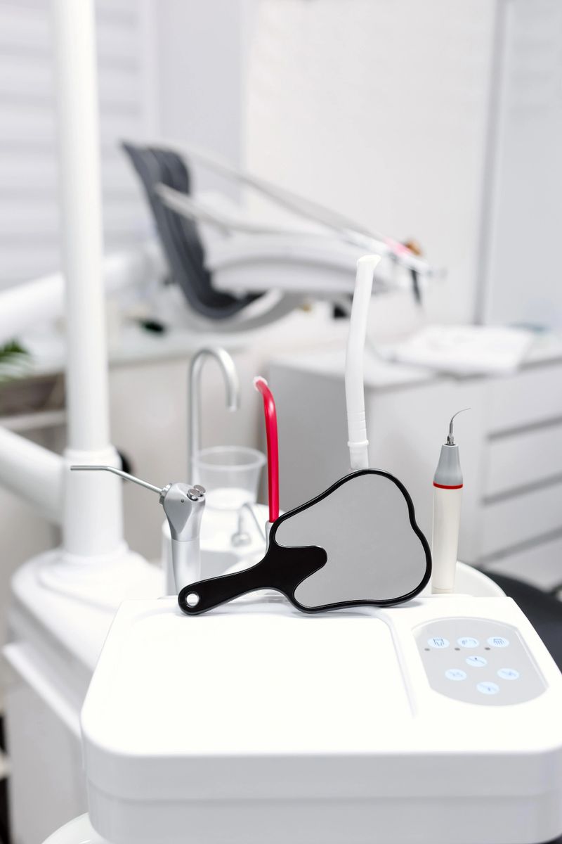 Dental unit with mirror and instruments in foreground inside bright modern dental treatment room.