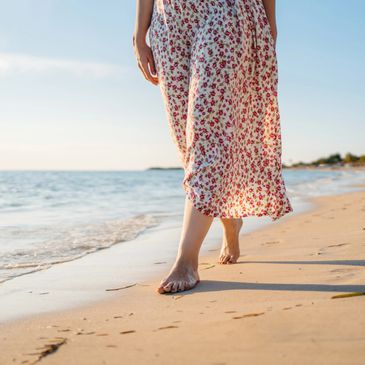 Person walking barefoot on a sandy beach wearing a floral dress.