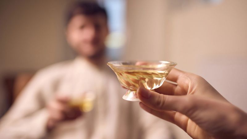 Hand holding glass cup of tea during quiet home tea ritual. Concept of everyday relaxation moments for wellness advertising, home comfort visuals, beverage promotion, and calm lifestyle imagery.