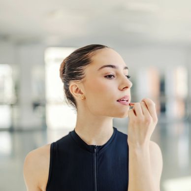 Woman applying lipstick in front of a mirror.