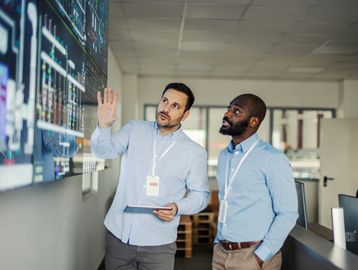 Two men analyzing data on a large screen in an office.